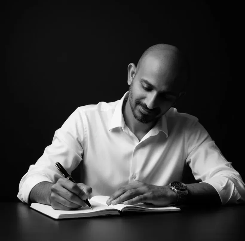 Zammy Zaif writing in a notebook at a desk, looking down at the page